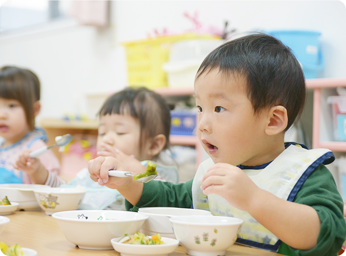 スプーンを使って給食の野菜を食べる子どもたち