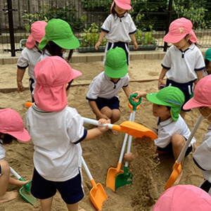園庭の砂場でスコップを使って遊ぶ子どもたち