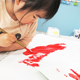 赤い絵の具を使って絵を描く子ども
